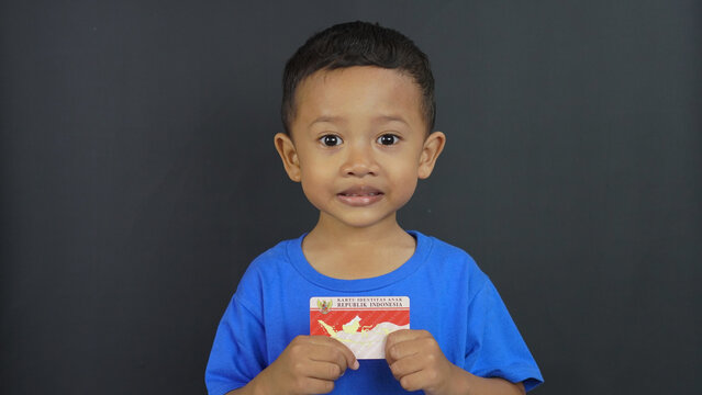 Little Asian boy holding the Republic of Indonesia Child Identity Card (KIA) or "Kartu Identitas Anak" in Bahasa, isolated on white background