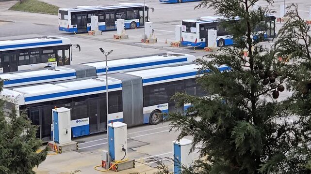 Aerial view of a large depot or parking lot for electric city buses, showing an articulated bus at a charging station with multiple charging points in the background. Varna. Bulgaria. 22.02.2026