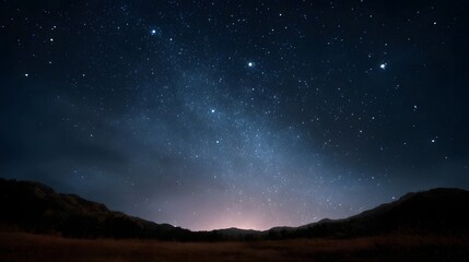 Obraz premium A breathtaking view of the Milky Way galaxy stretching across a dark starry night sky above silhouetted hills and a field of dry grass