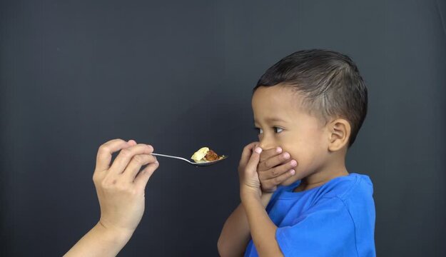 A small Asian boy is covering his mouth with both hands, a gesture of not wanting to eat anymore, known as GTM (Closed Mouth Movement), not wanting to continue eating from his mother