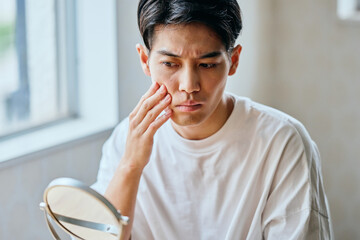 Fototapeta premium Asian young man checking his cheek skin in mirror