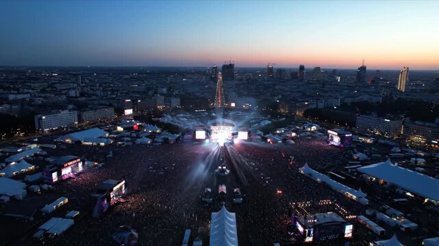 Aerial view of city skyline with crowd at outdoor music festival at dusk.