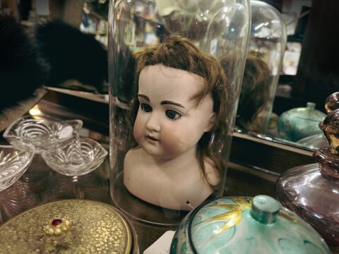 Creepy Victorian doll in a bell jar, on display in a vintage second-hand goods store.