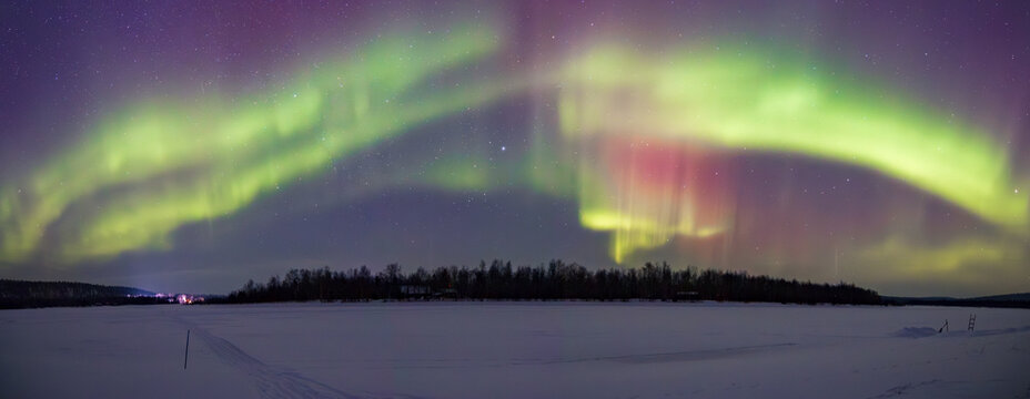 Stunning Aurora Borealis dancing over frozen Lake Inari and snowy forest in Ivalo, Finnish Lapland