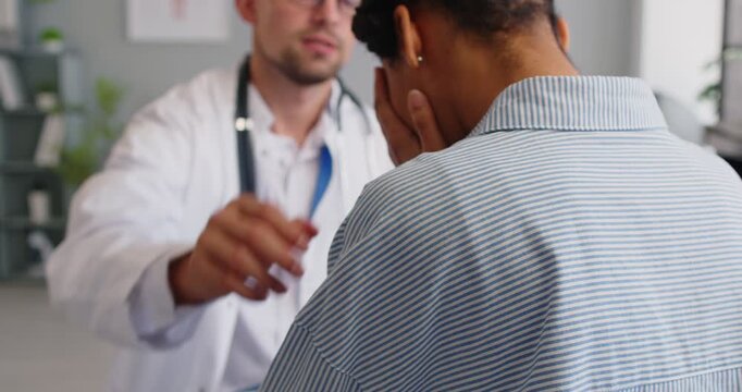 Support and assistance from doctor to patient during consultation at hospital. Sad woman talking about symptoms with anxiety and crying, man holding hand on shoulder and listening with empathy