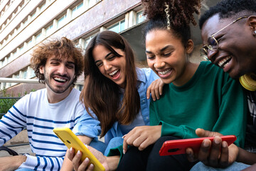 Diverse young friends laughing using mobile phones outdoors