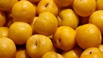 A pile of yellow plums fills the frame, each fruit displaying a smooth, round shape. The plums are closely packed together, showcasing their vibrant yellow hue