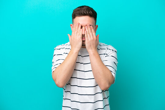 Young caucasian man isolated on blue background covering eyes by hands