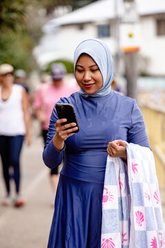 Filipina woman walking on coastal path holding a phone and a towel on the other hand