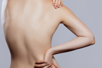 Fototapeta premium Women experiencing back pain while holding her back in a studio setting