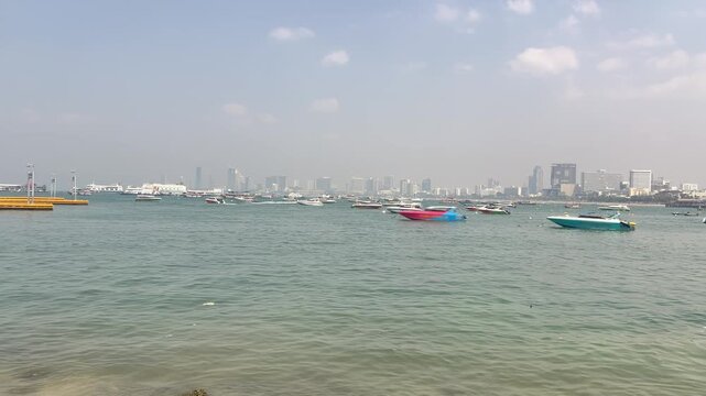 Colorful boats anchor calm harbor before skyscraper skyline. Urban towers rise hazy megacity waterfront panorama.