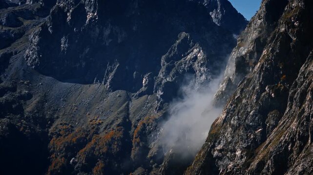 Aerial view of Montenegro high mountains Prokletije, scree slopes, and a narrow alpine valley as the camera pans, fog drifts, and autumn foliage clings