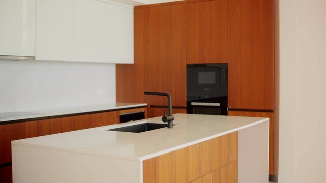 Slow lateral reveal shows white island with black sink and faucet, warm wood cabinets, white uppers, and built in black oven in Montenegro, in soft daylight.