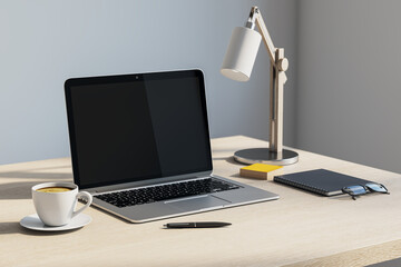 Modern laptop on clean office desk with lamp, coffee cup, notebook, glasses and pen in a...