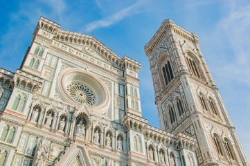 Fototapeta premium The intricate marble facade and Giotto's Campanile of the Florence Cathedral against a blue sky.