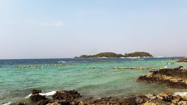 Tourist beach marked yellow buoys tropical island resort. Jet skis speed waves rocky shore background.
