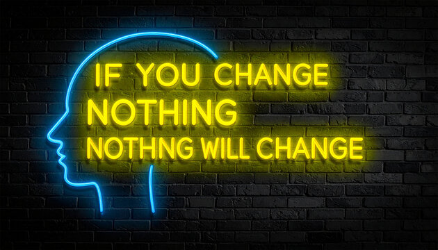 Leuchtende gelbe Neonschrift "if you change nothing, nothing will change" umramt von einem blauen Neongesicht auf dunkler Backsteinmauer