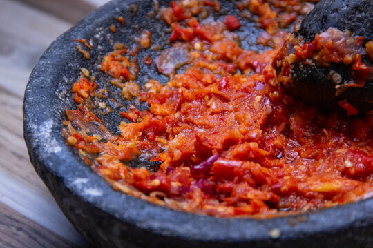 Freshly ground red chili paste (Sambal) in a traditional black stone mortar and pestle (cobek). Authentic Indonesian spicy condiment with visible chili seeds and texture.