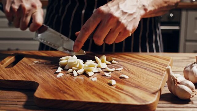 Hands Mincing Fresh Garlic on Wooden Cutting Board with Sharp Kitchen Knife
