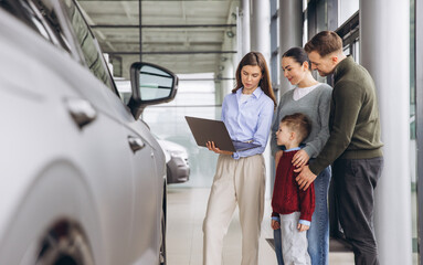 Obraz premium Salesperson assisting parents and their child choose a new car, explaining details on a laptop at an automobile dealership