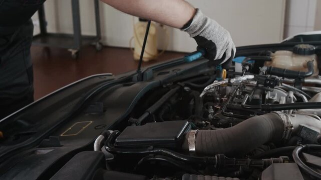 Medium close-up of hands of anonymous car mechanic, wearing gloves, changing spark plugs and replacing gaskets, then fixing bolts with wrench, while servicing motor vehicle engine in garage