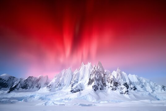 Snowy mountain range illuminated by red aurora borealis at dusk