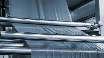 Automatic polyethylene plastic bag production machine with lighting effect. Close-up of the roller of the plastic bag production machine in the light blue scene. product packaging concept