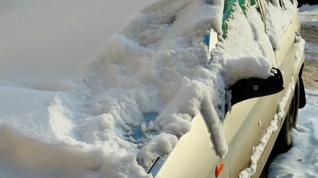 The snow-covered passenger car is completely covered with snow. The windscreen wipers, exterior mirrors, and door handles are all frozen with ice and covered with snow. Severe winter weather.
