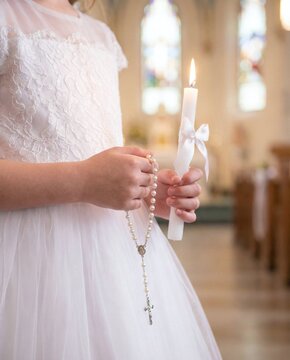 ai generated photo of a girl in a white lace dress holding a candle and rosary for first communion in church