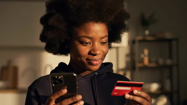 Smiling young African American woman holding smartphone and red credit card for mobile payment, concept for online shopping experience, digital finance management and ecommerce transaction