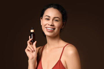 Young African-American woman with bottle of collagen on dark background