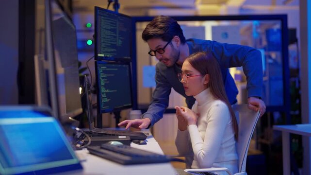 Asian programmers collaborating on software development at night, focused on writing code across multiple monitors in a tech office environment Programmers Collaborating on Software Development	