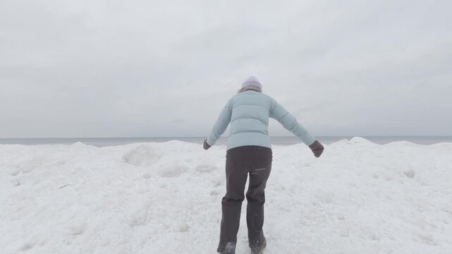 Walking on snowy shore towards frozen sea, back view of person in winter clothing, cold weather landscape, real life winter nature scene