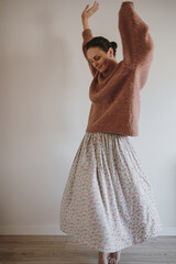 Woman Dancing Joyfully In Cozy Brown Sweater And Flowing Floral Skirt