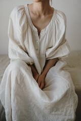 Woman Sitting In White Linen Dress With Puff Sleeves And Button Front In Minimal Room