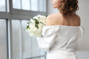 Beautiful bride with flowers near window in room, back view