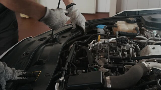 Medium shot of hands of two unrecognizable male car mechanic colleagues examining engine while servicing automobile in garage, pointing at spark plugs and cylinders to find reason for engine misfire