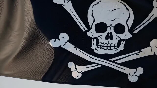 Black pirate flag with skull and crossbones waving in the wind, showcasing detailed design elements and textures against a clear blue sky backdrop