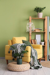 Obraz premium Comfortable armchair and book shelf near green wall in interior of living room, closeup