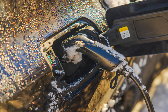 Close up view of electric car charging in winter with snow on body and cable connected. Sweden.