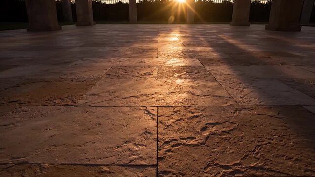 Sunlight casts long shadows across a textured stone patio at dusk