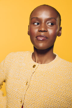 Confident African woman with dark skin wearing yellow knitted sweater looks sideways on yellow background. Portrait of natural beauty, fashion, and casual style with bright warm colors.
