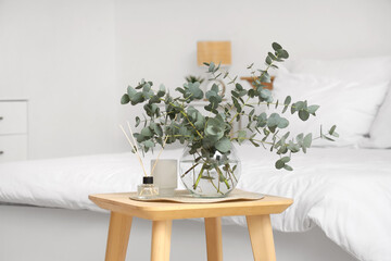Naklejka premium Glass vase with fresh eucalyptus branches on wooden table in bedroom