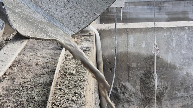 Extreme close-up of a concrete mixer truck chute end being rinsed with water, showing liquid pouring out.