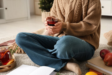 Woman with glass cup of hot mulled wine and fruits sitting on floor at home, closeup