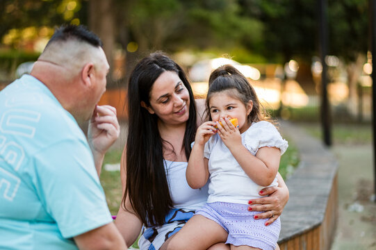 A parent and child share snacks while sitting in a park