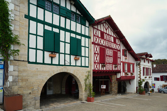 Traditional Basque houses with red timber frames and shutters along a picturesque street in the village of Ainhoa, France. A prime example of Labourd style architecture and cultural heritage