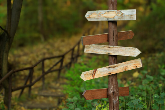 Wooden directional signpost in a forest with multiple weathered planks pointing different ways blurred background of autumn nature