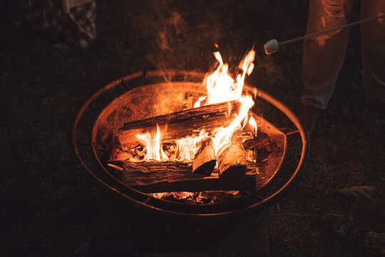 Burning wood logs in backyard fire pit at night with marshmallow