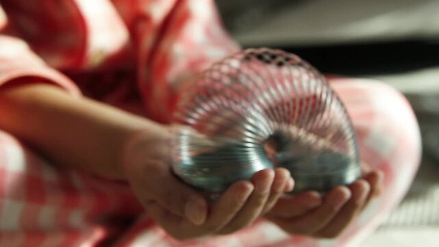 Child's Hands Playing with a Metal Toy Spring (Slinky)